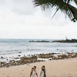 Bride and groom stroll on beach at Loulu Palm