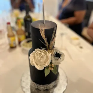 a black cake with white flowers and a single candle