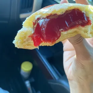 a hand holding a donut with jam on it