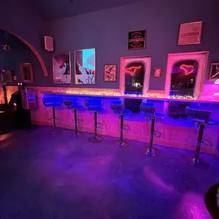 a bar with stools and neon lights