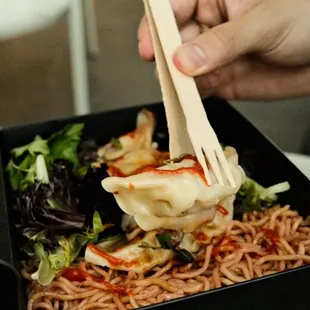 a person holding chopsticks over a bowl of noodles