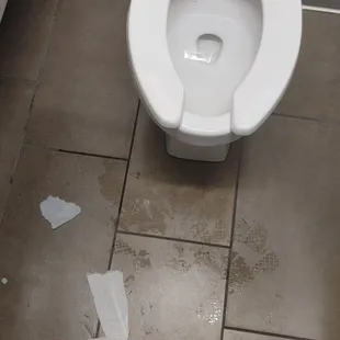 a toilet with toilet paper on the floor
