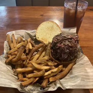 Brisket sandwich on a toasted bun, hand, sliced fries, and sweet tea