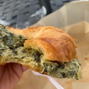 a hand holding a croissant sandwich