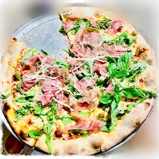 a pizza with meat and greens on it