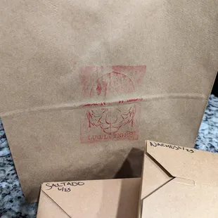 Lucha Tigre red-stamped brown paper leftovers bag with labeled boxes with dates. Thank you to our server Taryn for packing and labeling!