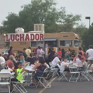 a large group of people sitting at tables in a parking lot