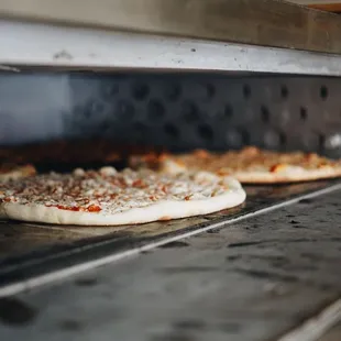 two uncooked pizzas cooking in an oven
