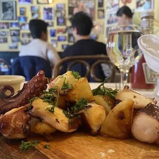 a plate of octopus and potatoes on a wooden cutting board