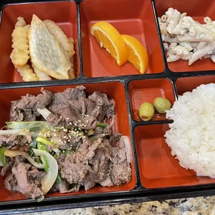 a bento box with rice, meat and vegetables