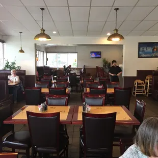The dining room is long, brightly lit, and displays the familiar dark wood chairs and tables with the beautifully embossed tops.