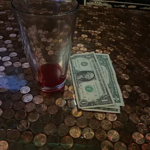 a glass of red liquid and a dollar bill on a table