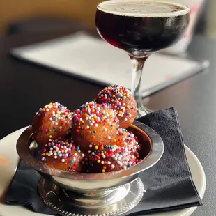 a bowl of donuts with sprinkles and a glass of wine