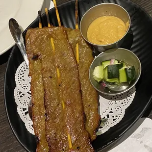 a plate of skewered meat and a bowl of sauce