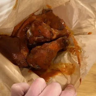 a hand grabbing a piece of chicken wings