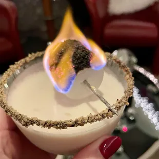 a close up of a person's hand holding a cocktail glass with a flaming on it