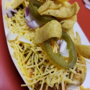 Chili dog topped with shredded cheese, onions, jalapenos and fritos
