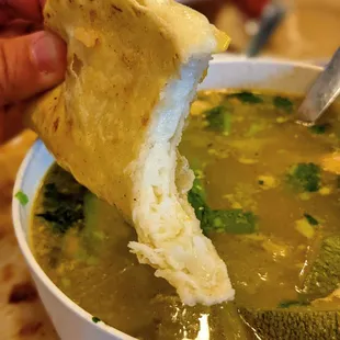 a person dipping a piece of bread into a bowl of soup