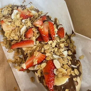 a chocolate covered donut with strawberries and granola
