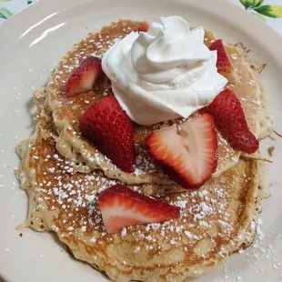 a stack of pancakes topped with whipped cream and strawberries