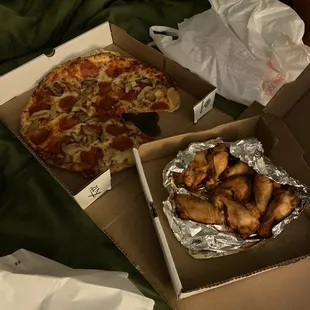 two pizzas in boxes on a bed