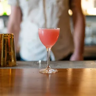 a bartender standing behind a bar with a pink drink