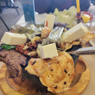 Fajita style bowl with strips of chicken and beef. The white cubes ontop is Mexican cheese. Also shrimp and saute vegetables.