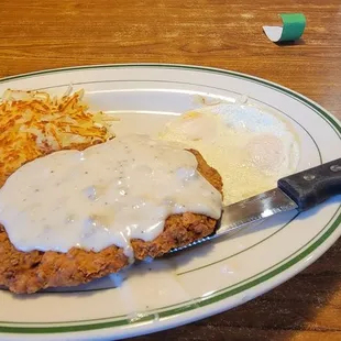 a plate of fried chicken with gravy and hash browns