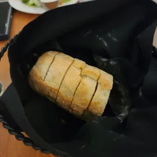 a loaf of bread in a basket with a salad in the background