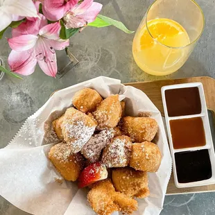 a bowl of powdered sugared donuts and a glass of orange juice