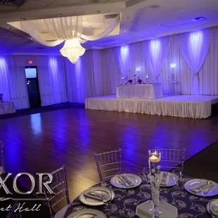 Large dance floor, stage with drapery and uplighting at the Luxor Banquet Hall. Quinceanera Reception in Dallas TX