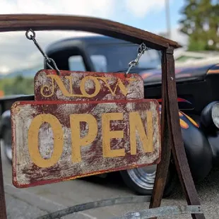 an old open sign in front of an antique car