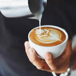 a person pouring milk into a cup of coffee