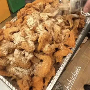 a person pouring salt onto a tray of fried chicken