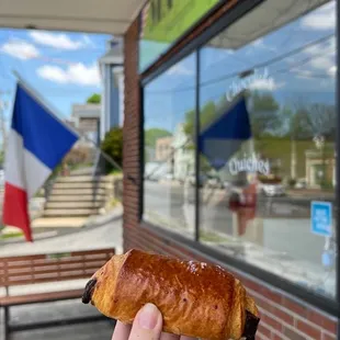 a person holding a pastry in front of a store