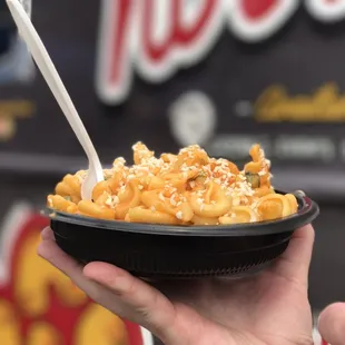 a hand holding a bowl of macaroni and cheese