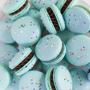 a plate of blue macarons with chocolate and sprinkles