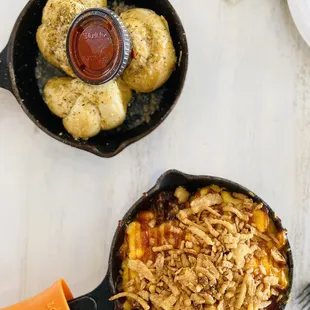 Cast iron skillet with burnt ends Mac &amp; Cheese topped with onion straws and a cast iron skillet with 3 garlic knots with a side of marinara.