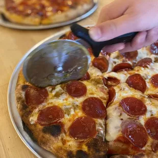 a person cutting a pepperoni pizza