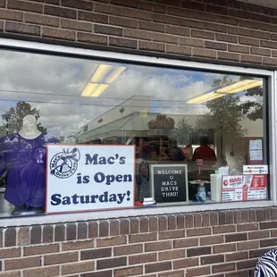 a window with a sign that says mac's is open saturday