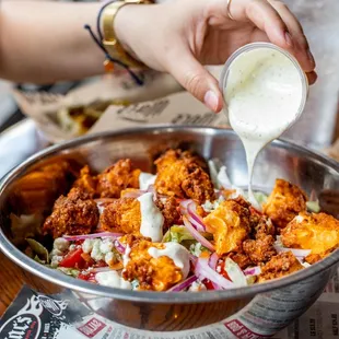 a person pouring dressing into a bowl of food