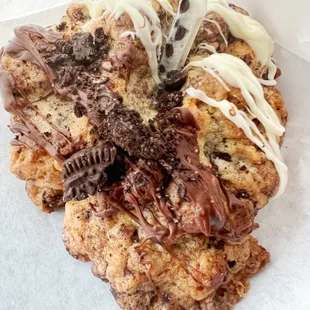 Cruella: Chocolate chip cookie with pieces of Oreo cookie, white chocolate drizzle, and topped with a piece of Cookies and Creme bar