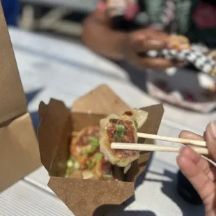 a person holding chopsticks over a box of food