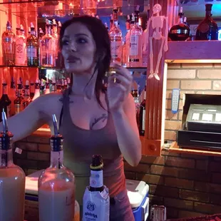 a woman standing behind a bar with bottles of alcohol