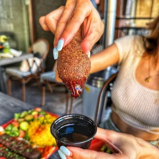 a woman dipping a piece of meat into a bowl of sauce