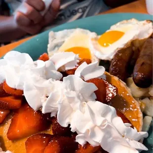 a plate of pancakes with whipped cream and strawberries
