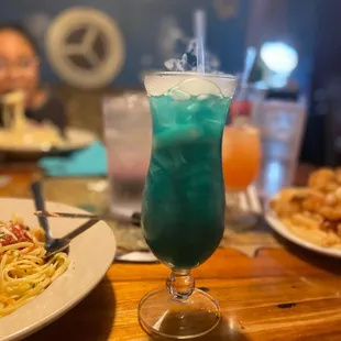 a blue drink and pasta on a table