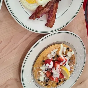 Lemon poppyseed waffle with blueberries and strawberries on top Over medium eggs and crispy bacon