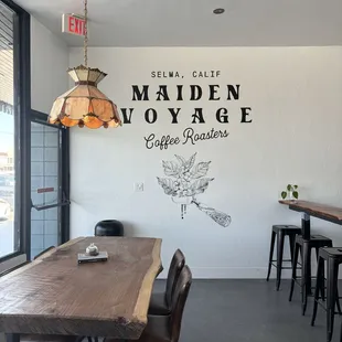 To the left: Table and chairs by window To the right: an L shaped bar with stools