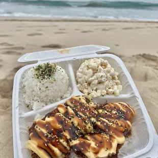  hand holding a takeout container of food on the beach